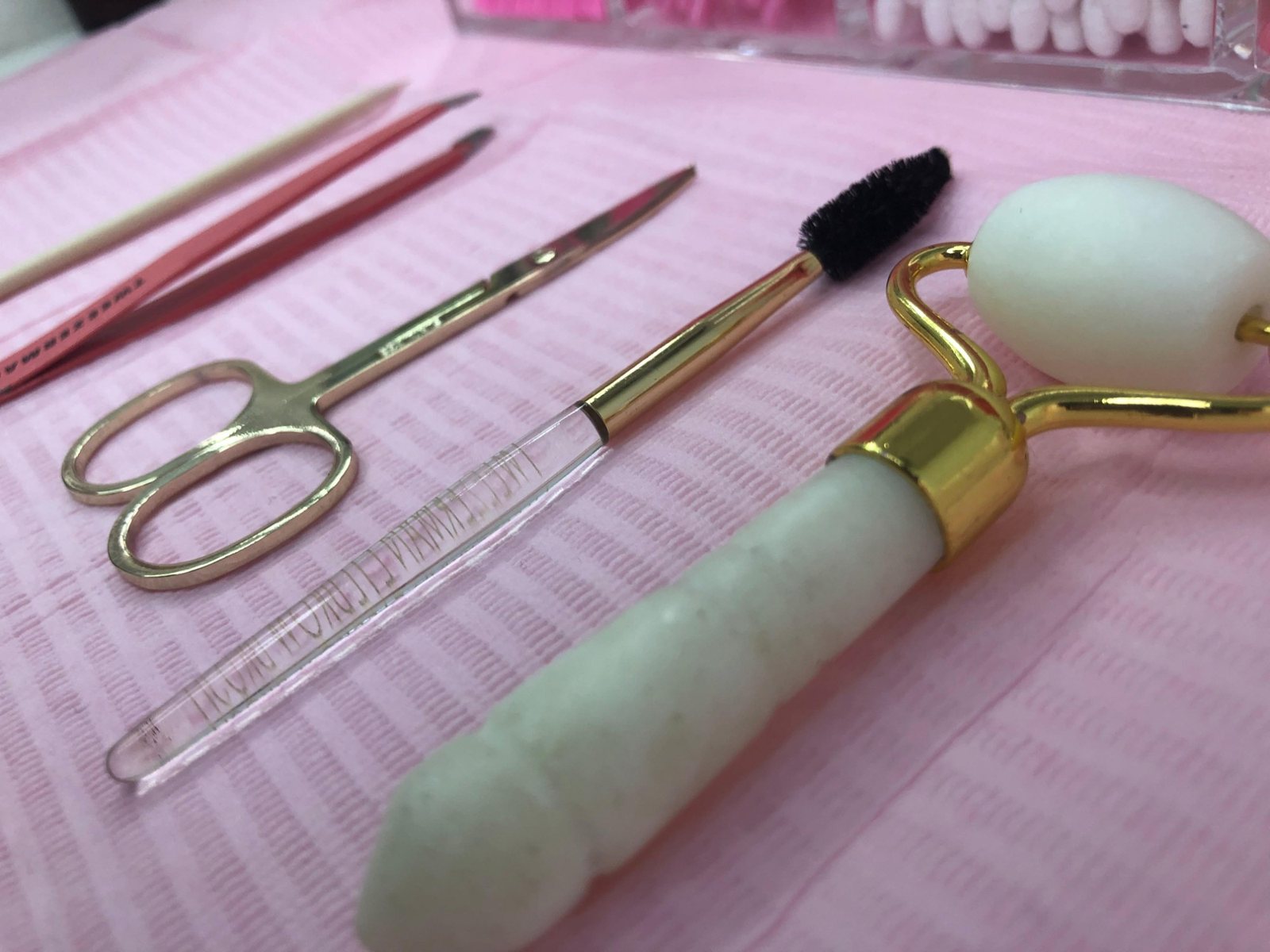 Brow tools on a pink tray: tweezers, scissors, a spoolie and a face roller